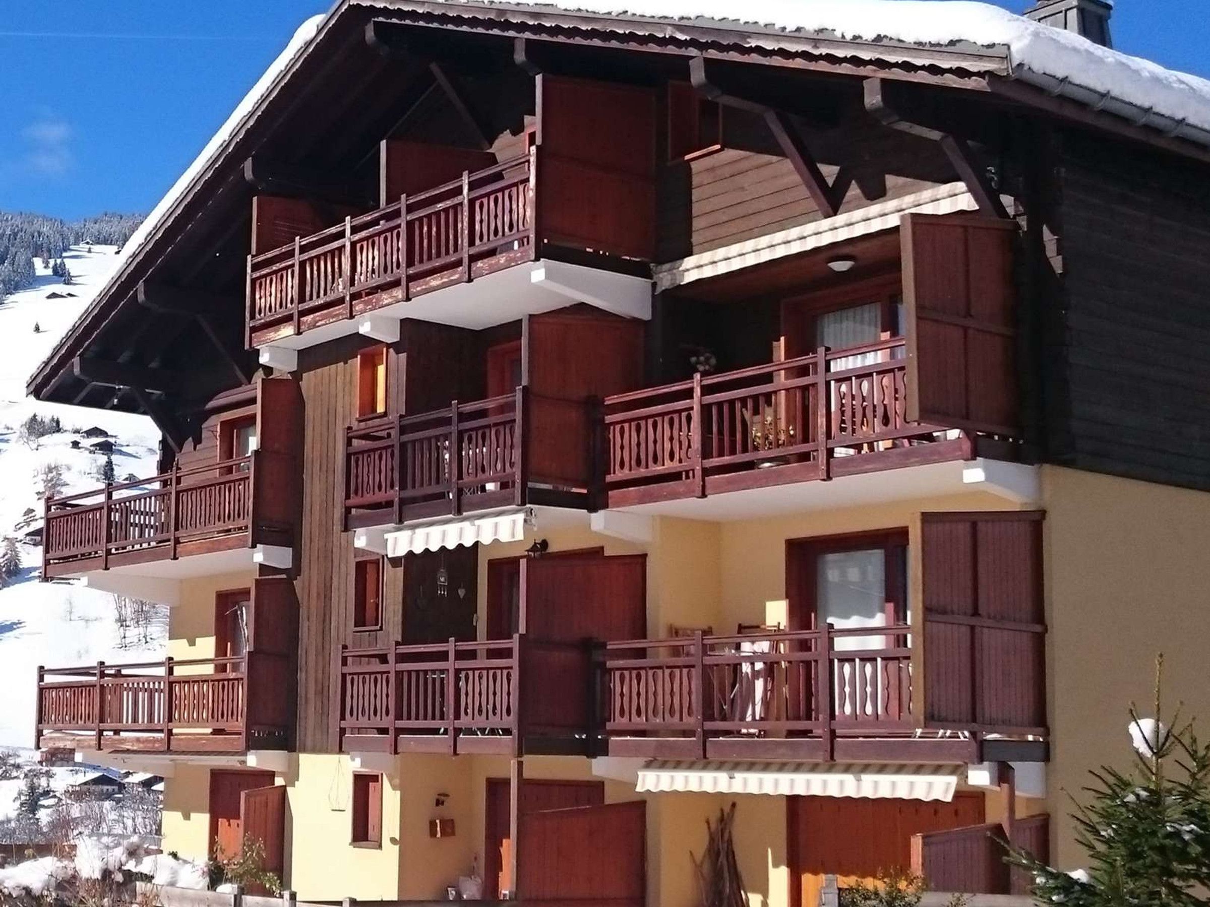 A multi-story chalet with wooden balconies and a ski slope in the background.