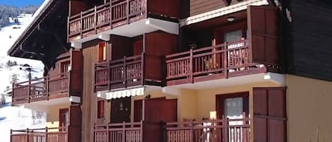 Una chaleta de varios pisos con balcones de madera y una pista de esquí al fondo.