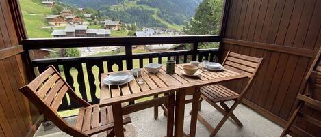 Une table et des chaises en bois sur un balcon avec vue sur la montagne.