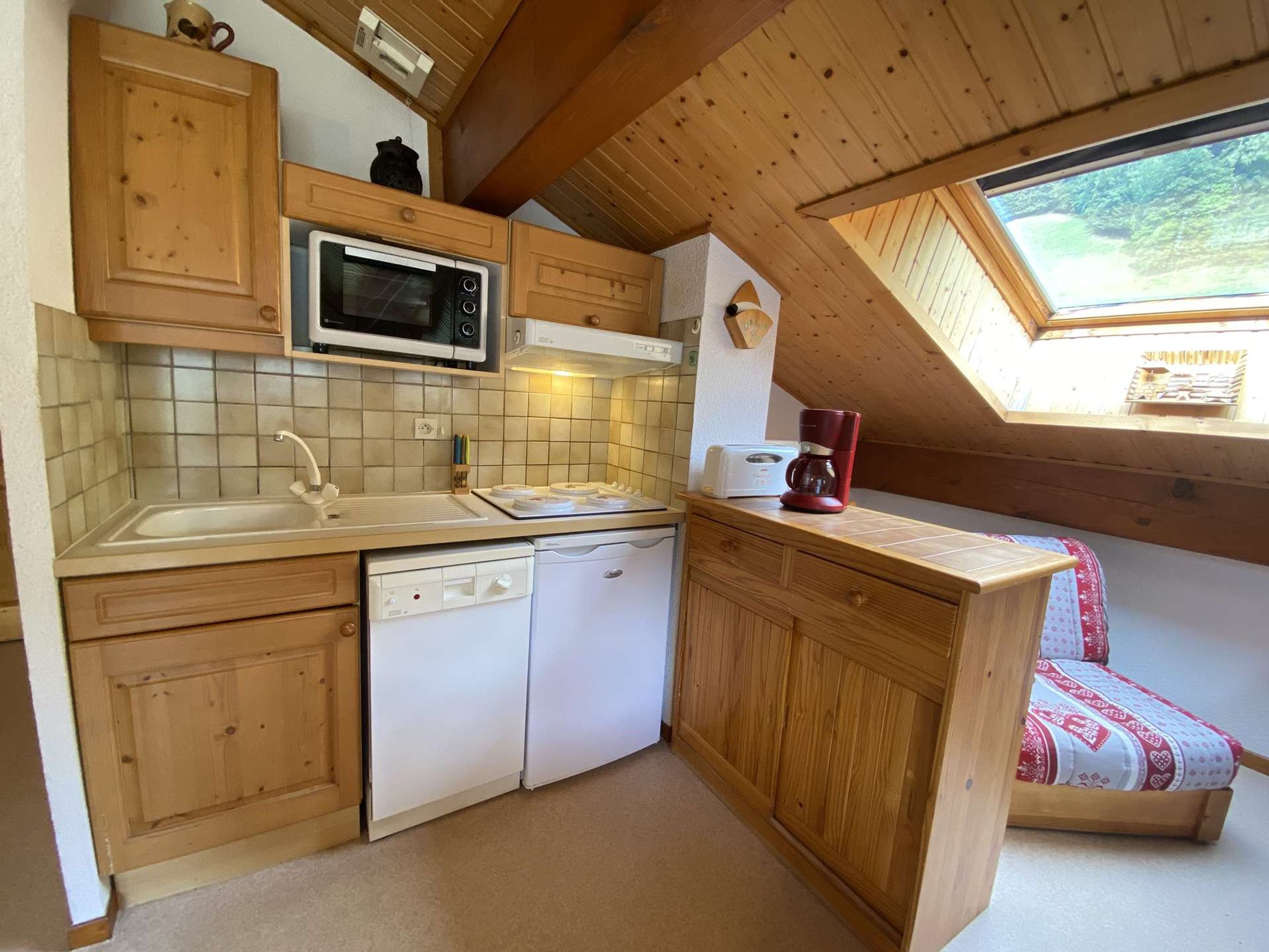 Une cuisine compacte avec des meubles en bois, un four à micro-ondes, un lave-vaisselle et une petite fenêtre.