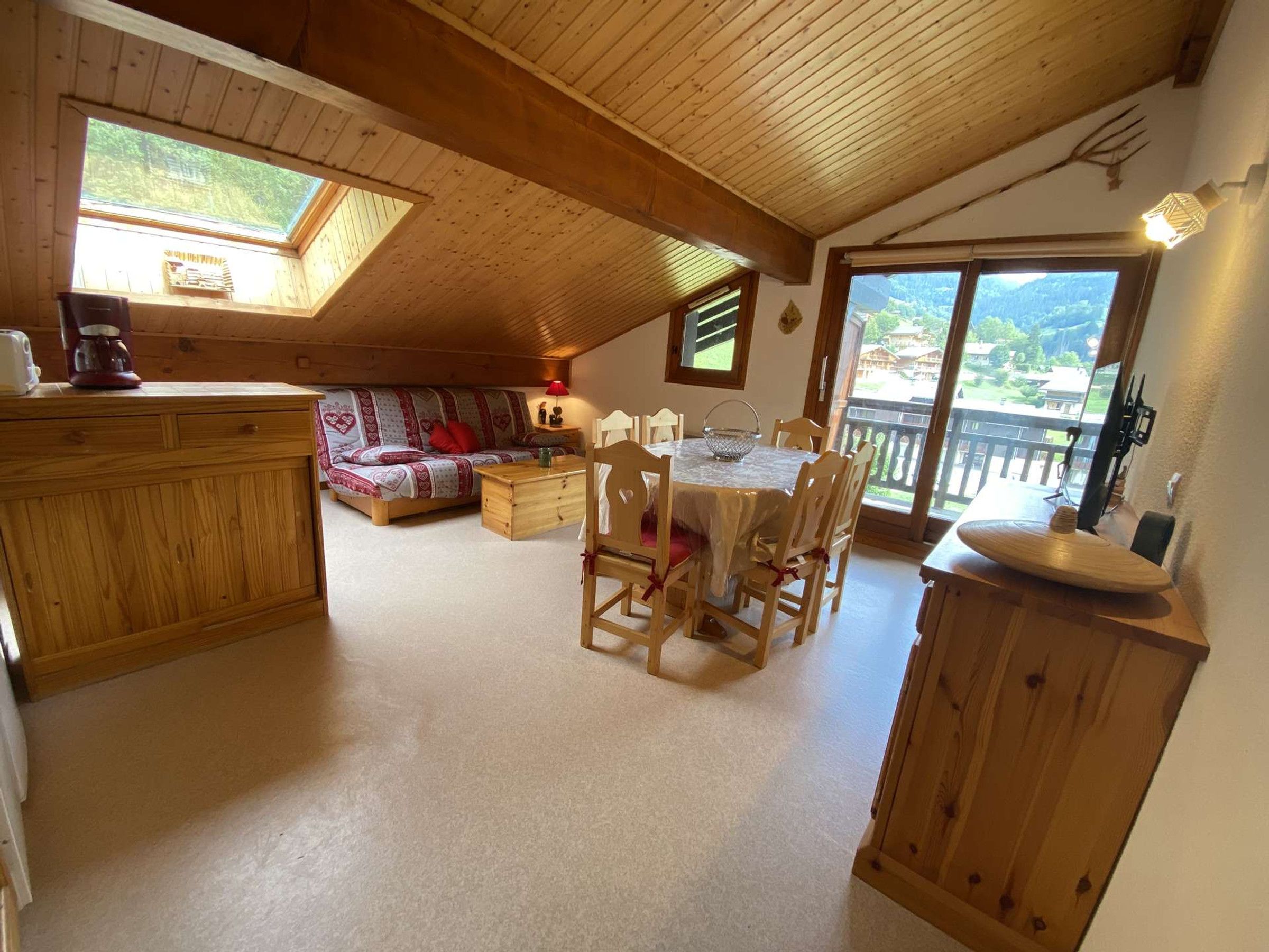 Une pièce chaleureuse avec un plafond en bois, une table à manger avec des chaises, un canapé et un coin cuisine doté d’un meuble en bois.