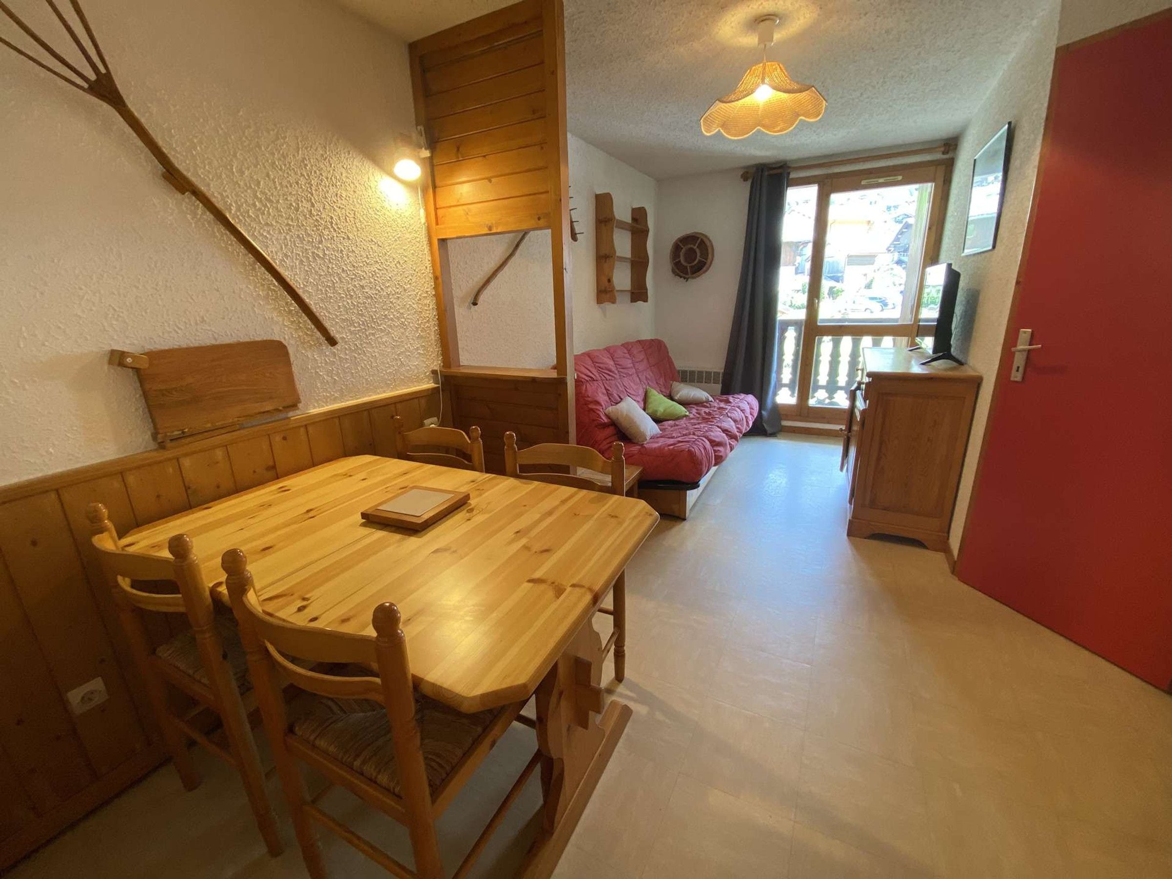 Un coin repas avec une table et des chaises en bois, un canapé rouge et un espace cuisine avec des placards.