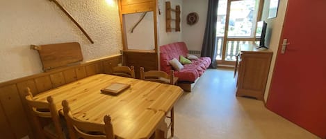 Un comedor con una mesa y sillas de madera, un sofá rojo y una zona de cocina con armarios.