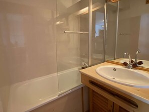 Ein Badezimmer mit Duschkabine aus Glas, einem weißen Waschbecken mit Holzschrank und einem Spiegel über dem Waschbecken.