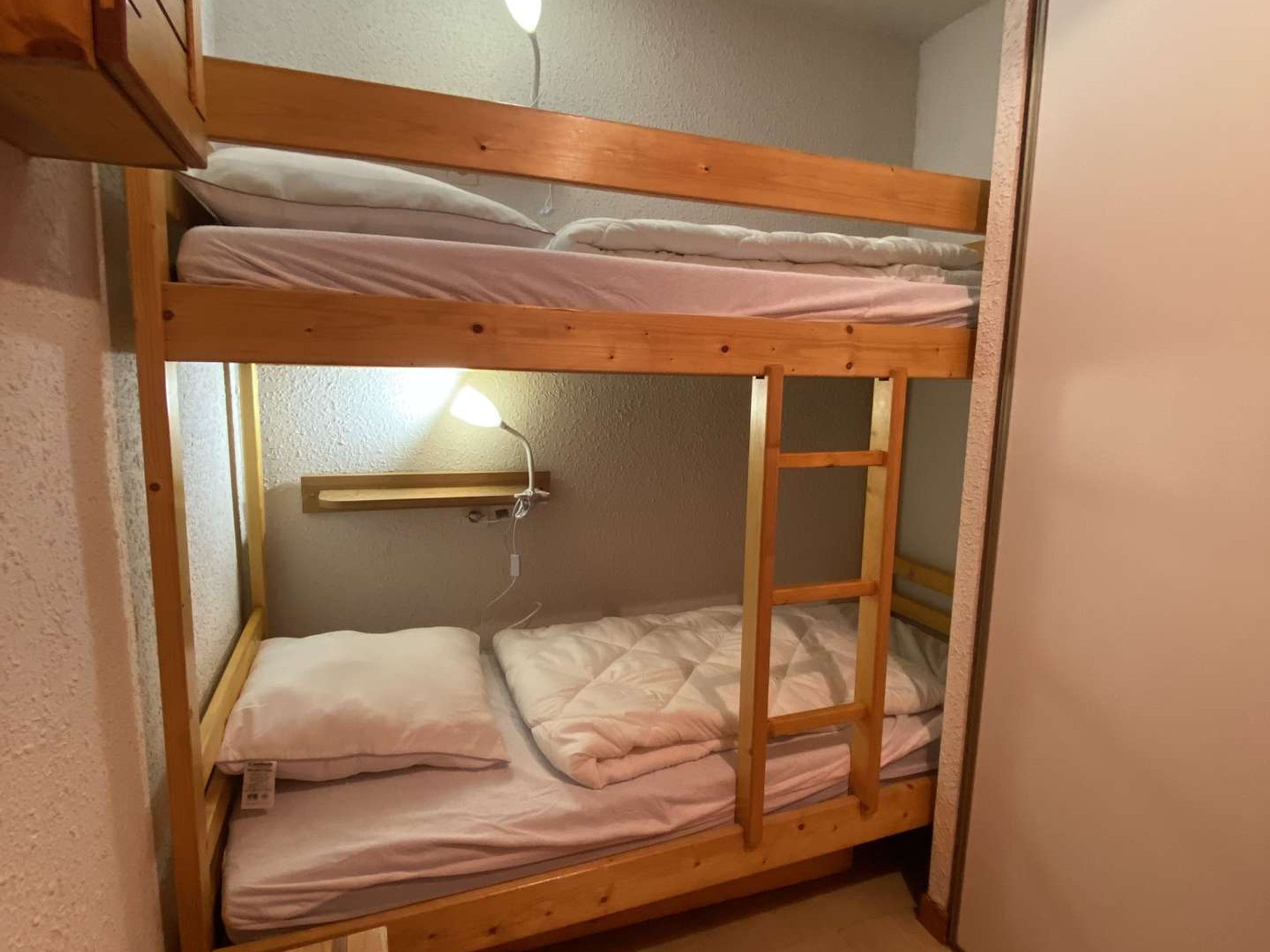 A bunk bed with a ladder, a shelf, and a bedside lamp.