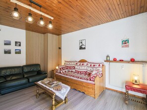 A cozy room with a wooden ceiling, a wooden bed with patterned bedding, a leather sofa, a small table with books, and wall-mounted pictures. - Pleasant apartment, mountain view - 6 guests (Villard-de-Lans)
