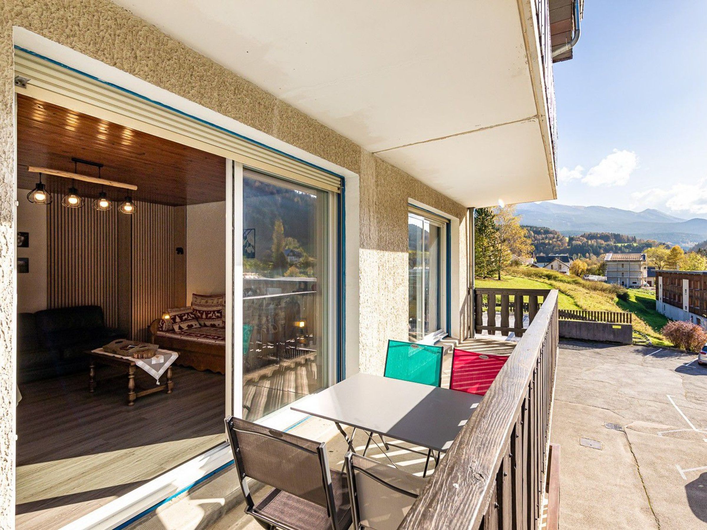 A balcony with a table and chairs, a wooden deck, and a view of a mountainous landscape.