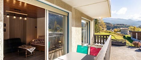 A balcony with a table and chairs, a wooden deck, and a view of a mountainous landscape.