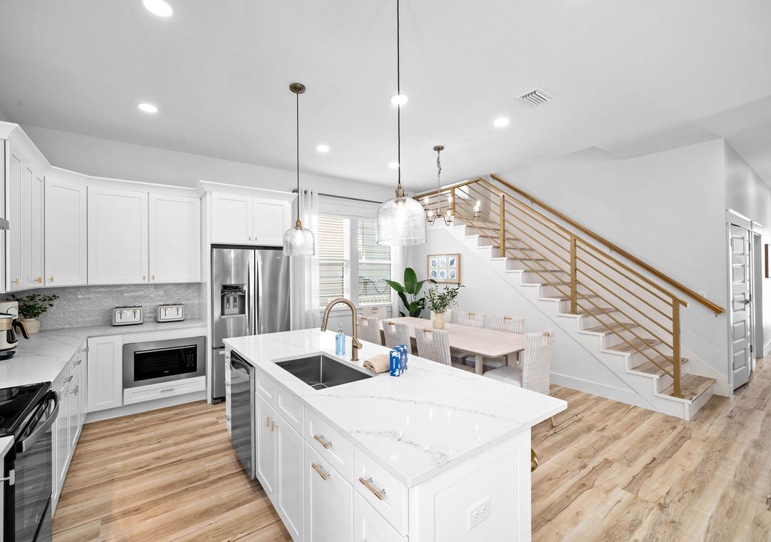 Una cocina moderna con armarios blancos, una isla central, electrodomésticos de acero inoxidable y una escalera de madera.