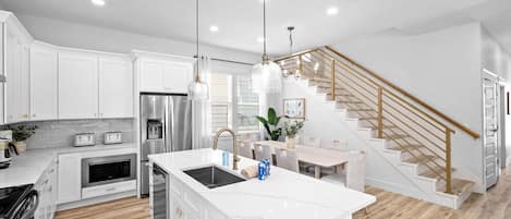 Una cocina moderna con armarios blancos, una isla central, electrodomésticos de acero inoxidable y una escalera de madera.