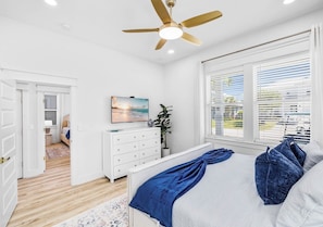 A bedroom with a bed, a ceiling fan, a dresser, a painting, and a window with blinds. - Blue Lagoon: Private beach access, FREE Golf cart, Heated pool, Arcade Room (Miramar Beach)