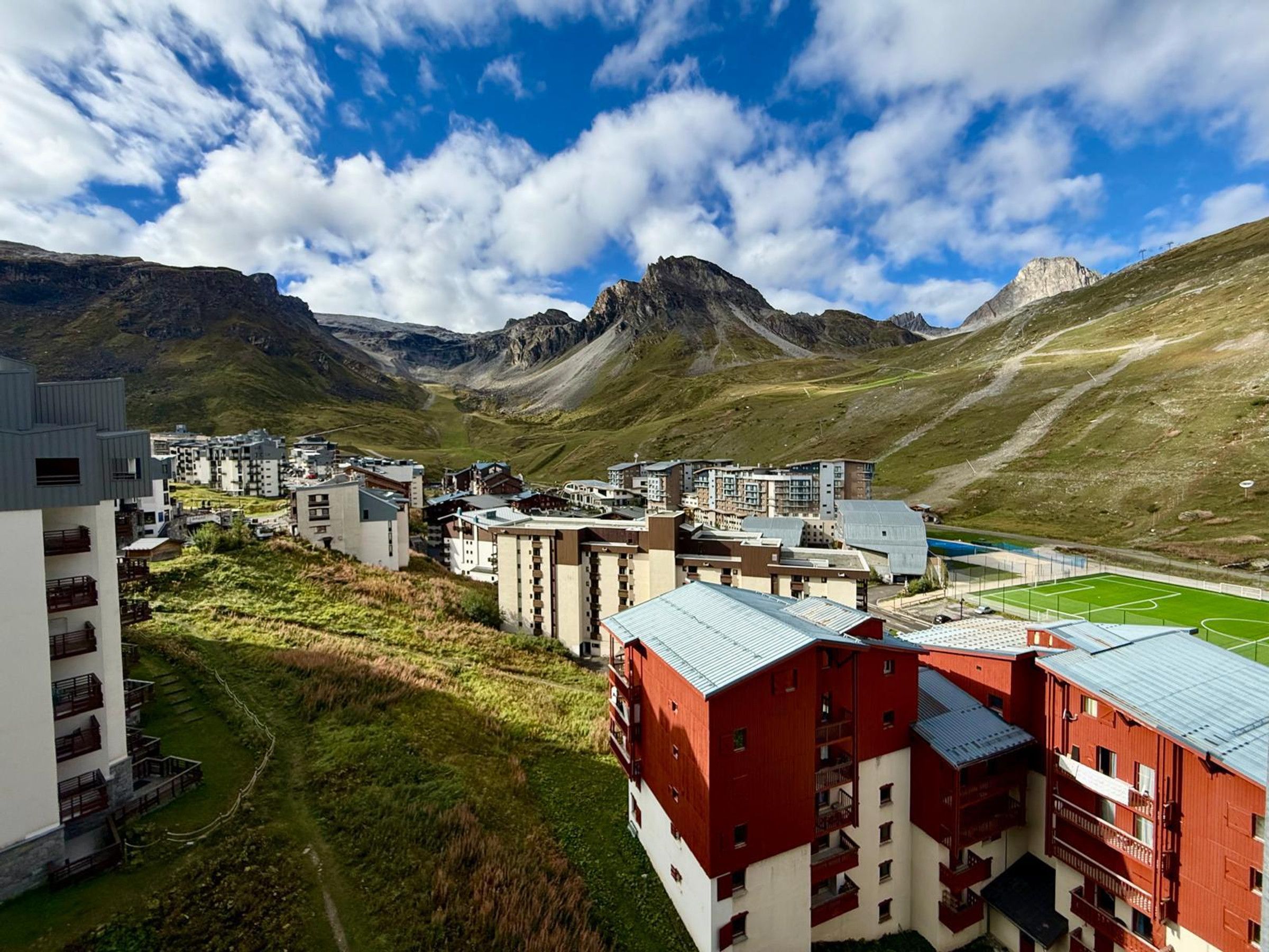 A mountainous area with buildings, including a red and white structure, and a sports field.