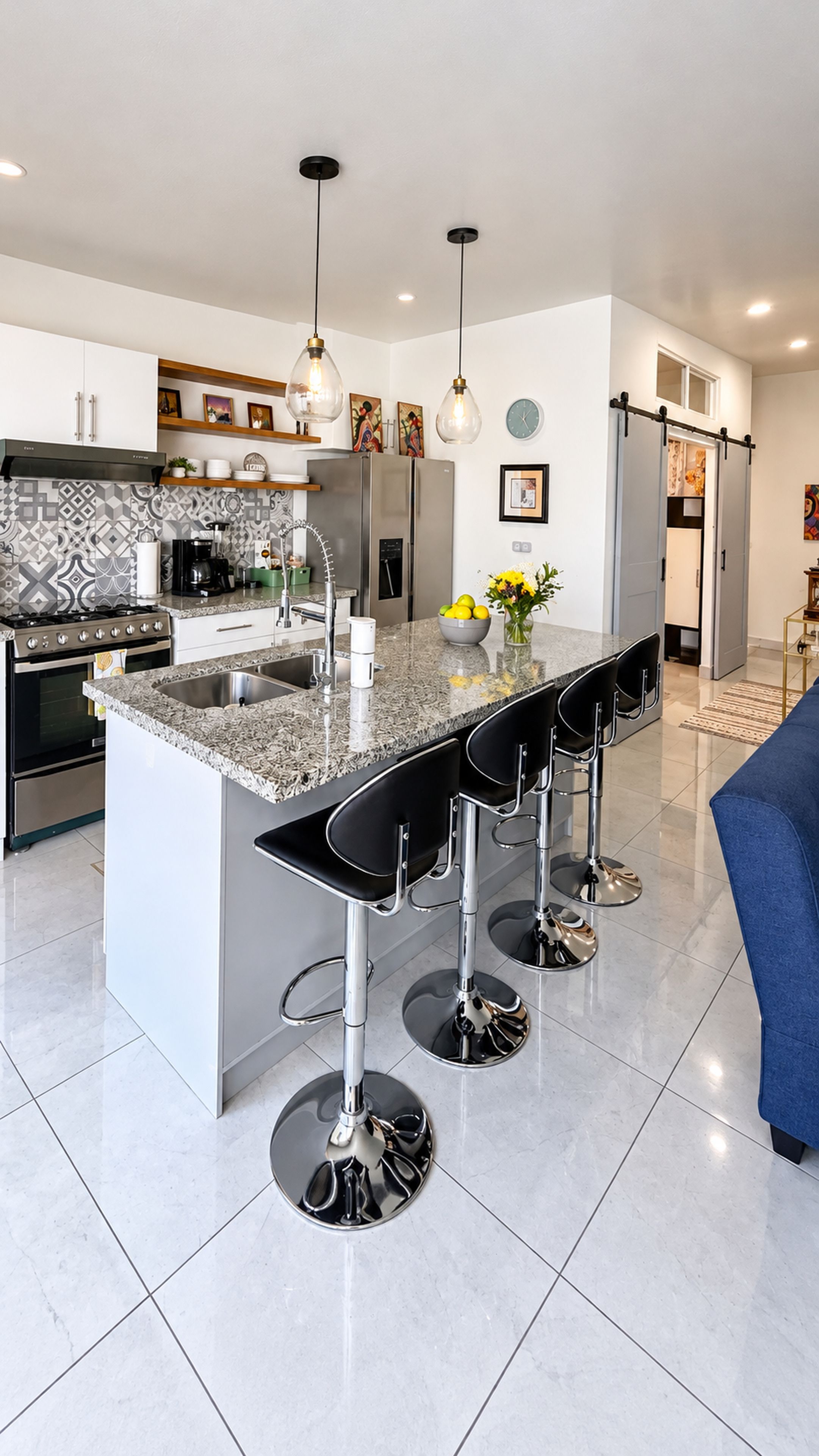 A modern kitchen with a central island, bar stools, stainless steel appliances, and pendant lighting.