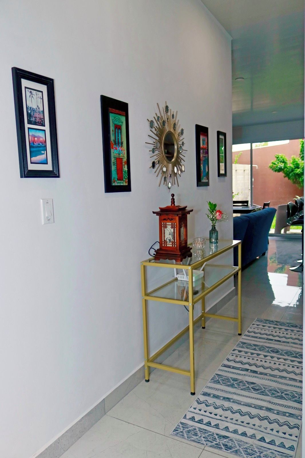 A hallway with a glass-top console table, framed pictures, and a decorative mirror.