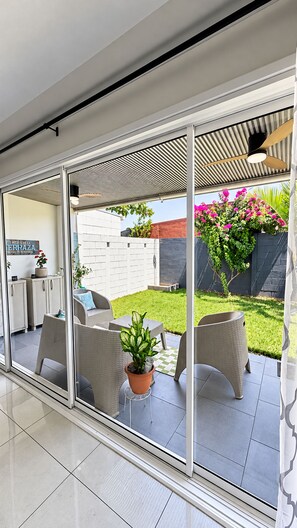 Un espace patio moderne avec une porte vitrée donnant sur un jardin, des meubles d’extérieur et une plante en pot.