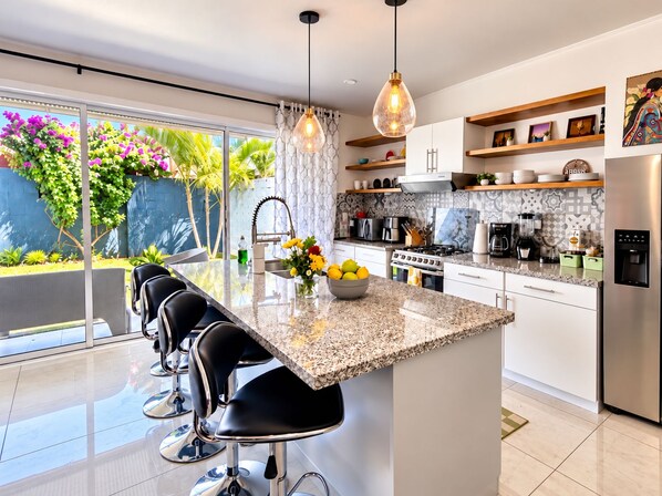 A modern kitchen with a central island, bar stools, stainless steel appliances, and a view of a garden.