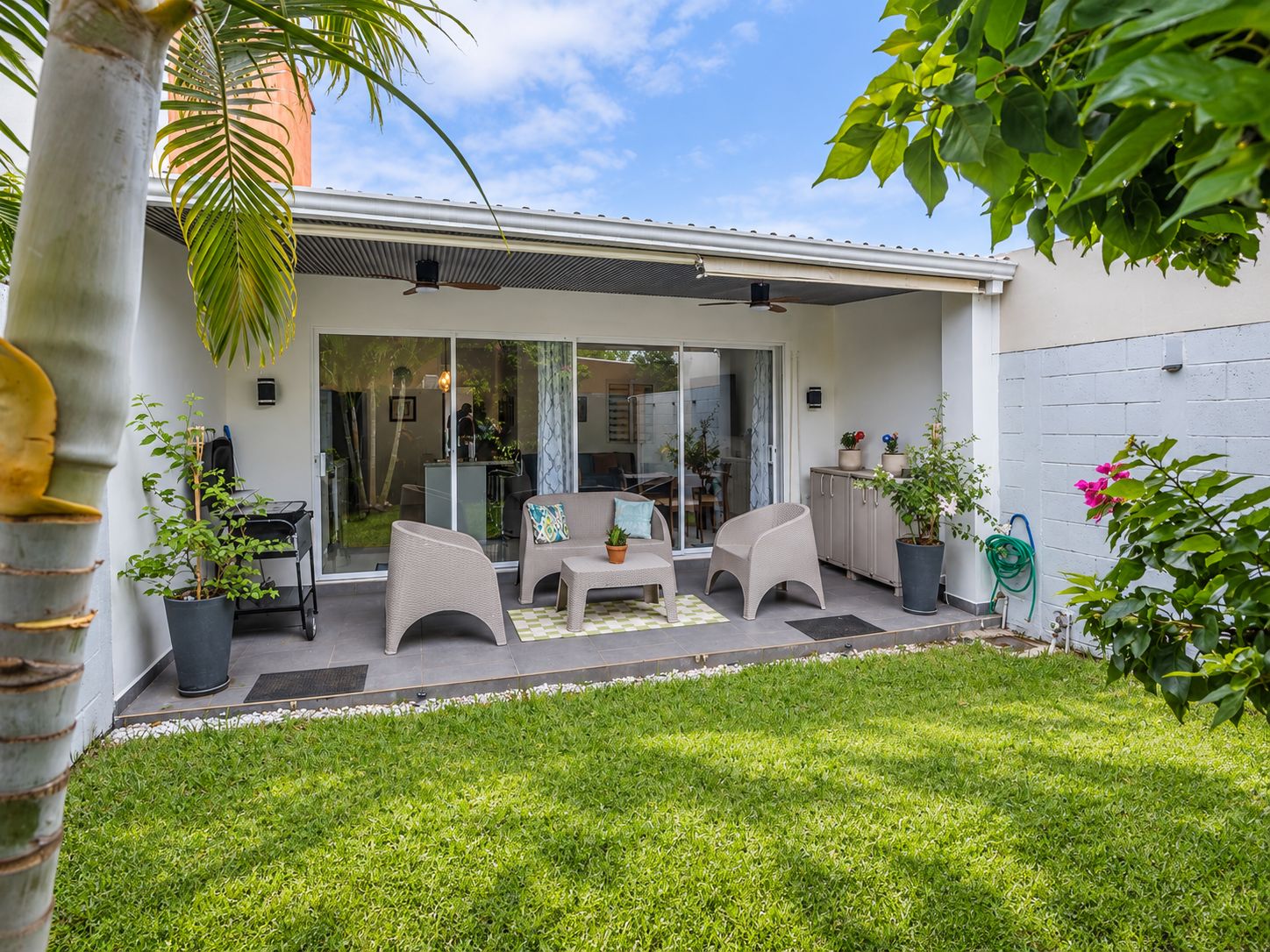 Une terrasse moderne avec des meubles d’extérieur, une porte vitrée donnant sur un espace abrité et une pelouse bien entretenue.