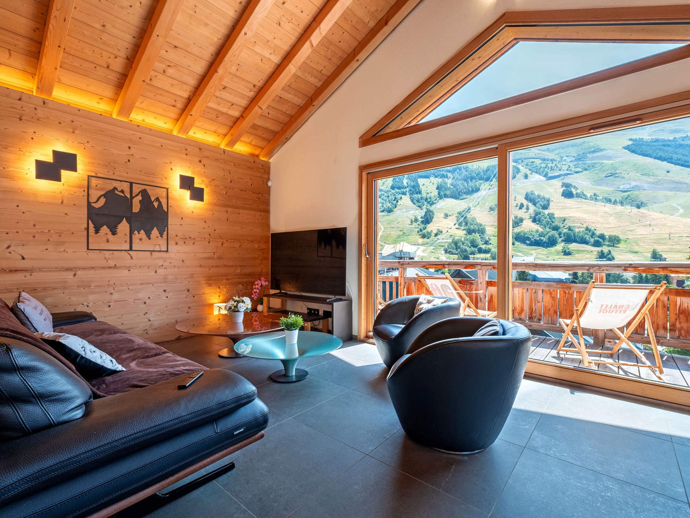 A modern interior with a wooden ceiling, a sofa, a TV, and a balcony with a scenic view.