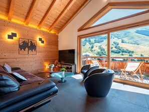 A modern interior with a wooden ceiling, a sofa, a TV, and a balcony with a scenic view. - Spacious chalet, panoramic view - 8 guests (Les Deux Alpes)
