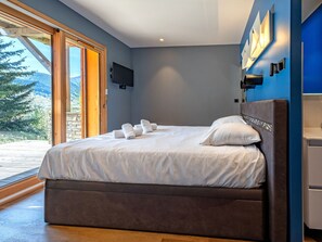 A bedroom with a large bed, a television mounted on the wall, and a view of the outdoors. - Spacious chalet, panoramic view - 8 guests (Les Deux Alpes)