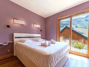 A bedroom with a large bed, two bedside lamps, and a view of a landscape through a large window. - Spacious chalet, panoramic view - 8 guests (Les Deux Alpes)