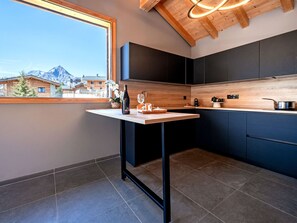 Une cuisine moderne avec un plan de travail en bois, des meubles sombres et une vue sur les montagnes par une grande fenêtre.