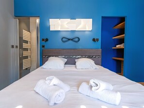 Une chambre d’hôtel avec un lit, deux oreillers, une tête de lit, un luminaire fixé au mur et une serviette sur le lit.
