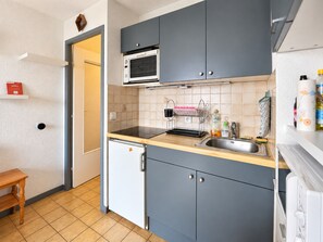 Cozinha compacta com armários cinzas, micro-ondas, pia e uma geladeira pequena.