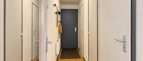 A hallway with doors on both sides, a dark door at the end, and a light-colored wall with a textured finish.