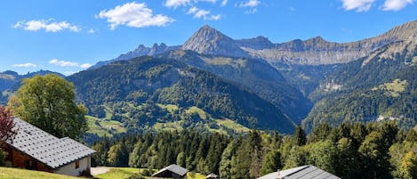 Un paysage de montagne avec un ciel dégagé, quelques bâtiments aux toits inclinés et des collines densément boisées.