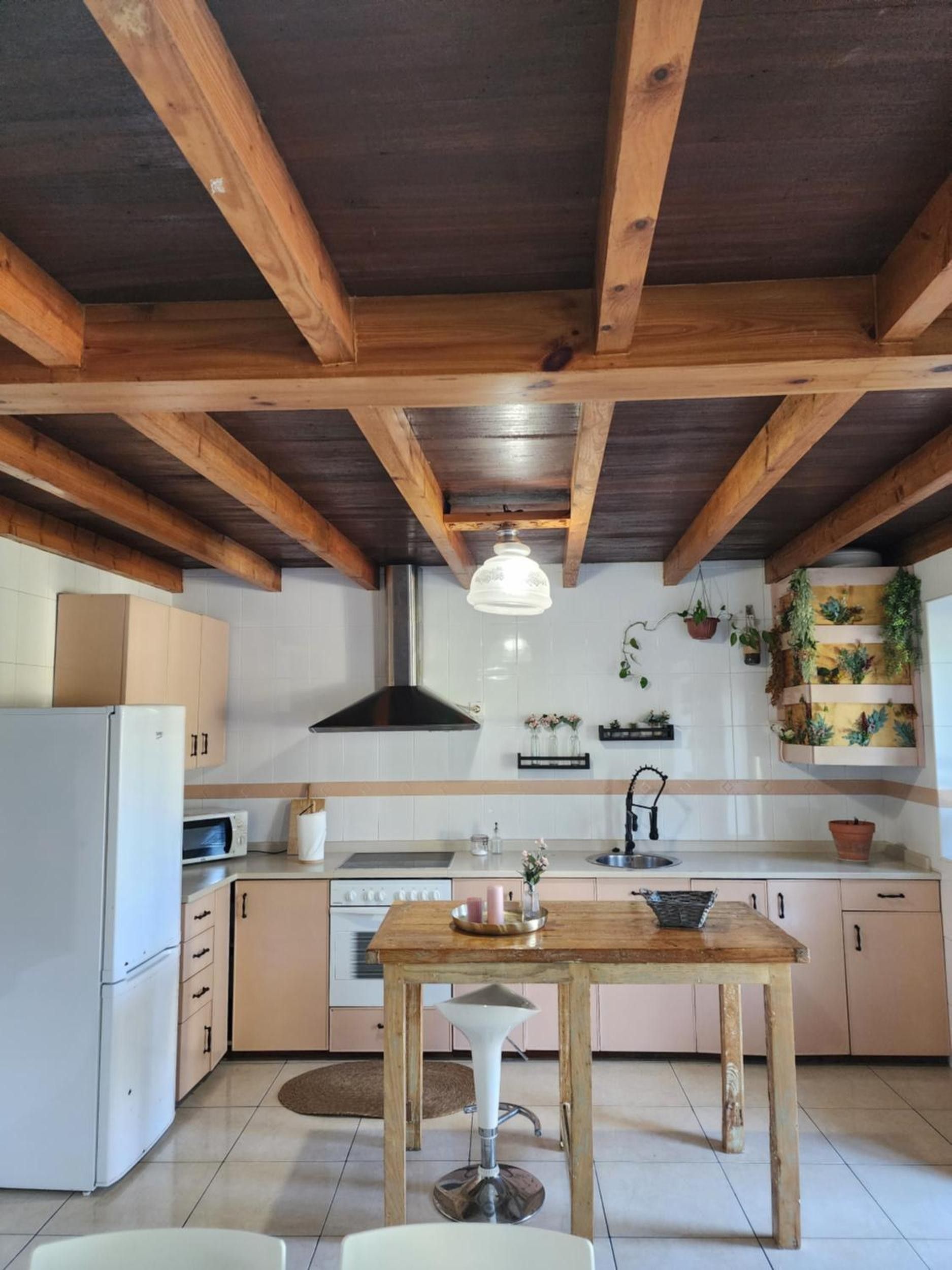 A kitchen with wooden beams, a white refrigerator, a stove, and a hanging light fixture.