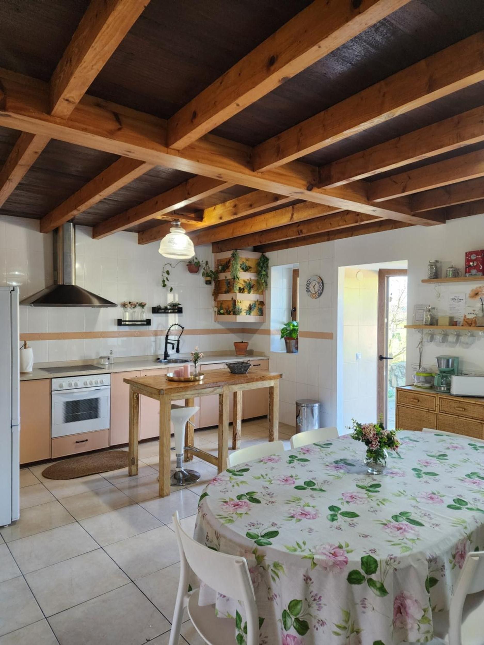 Una cocina con vigas de madera, estufa, lavamanos y una mesa de comedor con mantel floral.