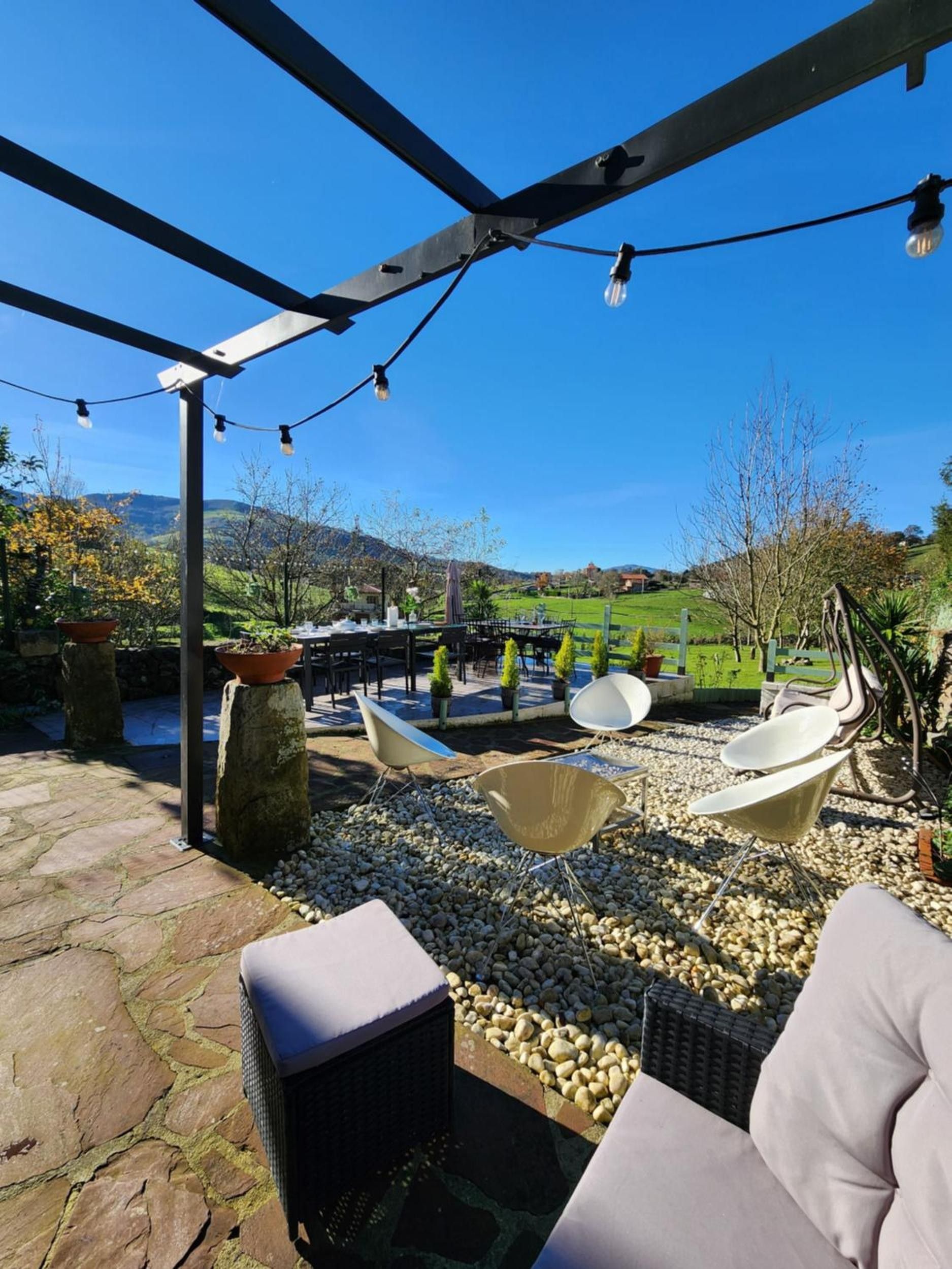 Eine Außenpatio mit Steinböden, einer Pergola, Lichterketten und Gartenmöbeln.