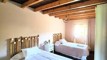 Une chambre avec deux lits, des poutres en bois au plafond, un luminaire suspendu et une fenêtre avec des rideaux.
