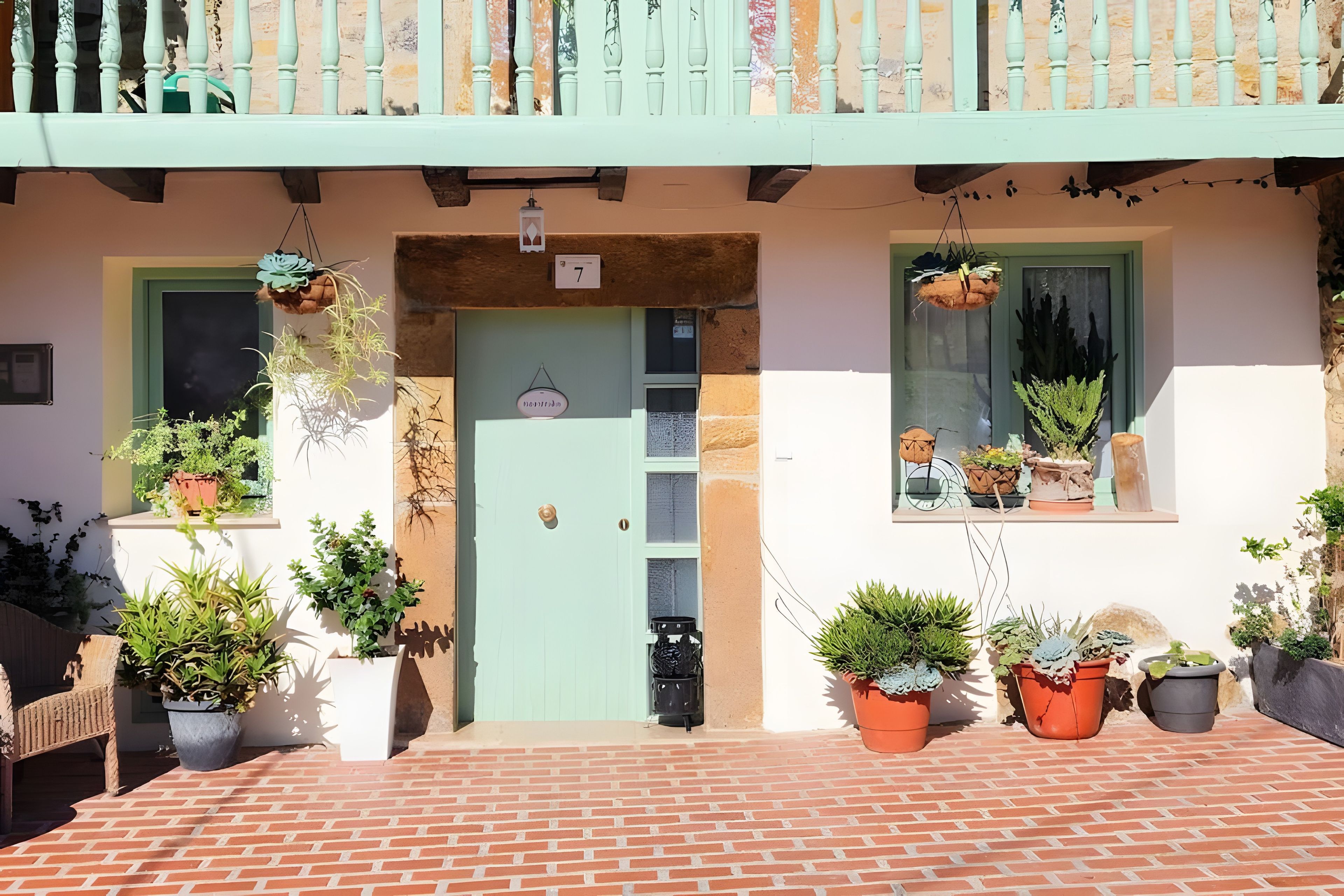 A building with a green door, multiple potted plants, and a balcony with a railing.