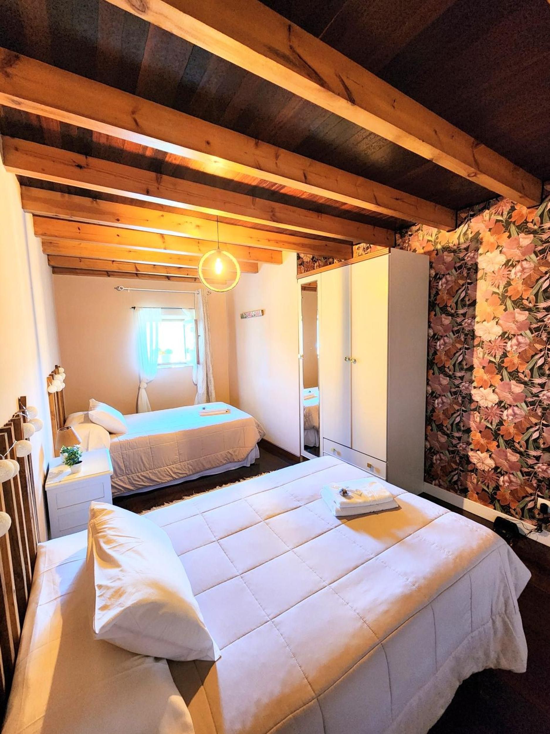 Ein Schlafzimmer mit zwei Betten, einem Kleiderschrank, einem Spiegel und floralem Wandpapier.