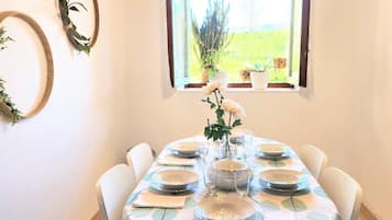 Een eetgedeelte met een tafel voor vier personen, omringd door witte stoelen, onder een houten plafond met zichtbare balken.