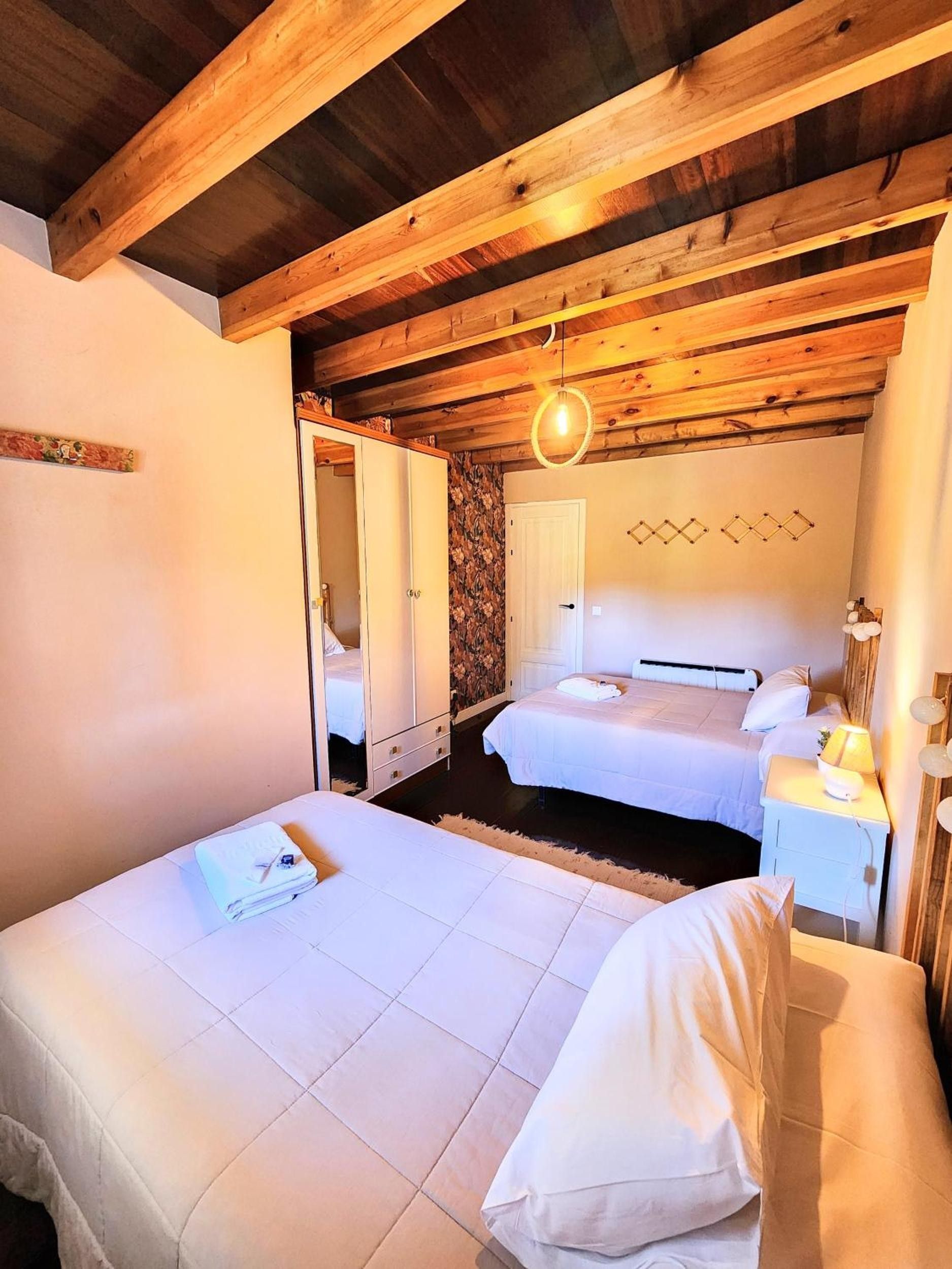 Una habitación con dos camas, vigas de madera en el techo, una puerta blanca y una lámpara fijada a la pared.