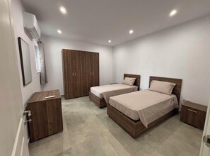 A bedroom with two beds, a wardrobe, and a bedside table.