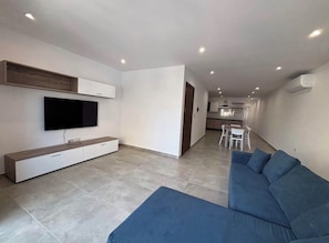 A modern living room with a flat-screen TV, a sofa, and a dining area in the background.