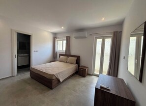 A bedroom with a bed, bedside table, and a small cabinet. There is a sliding door leading to a balcony.