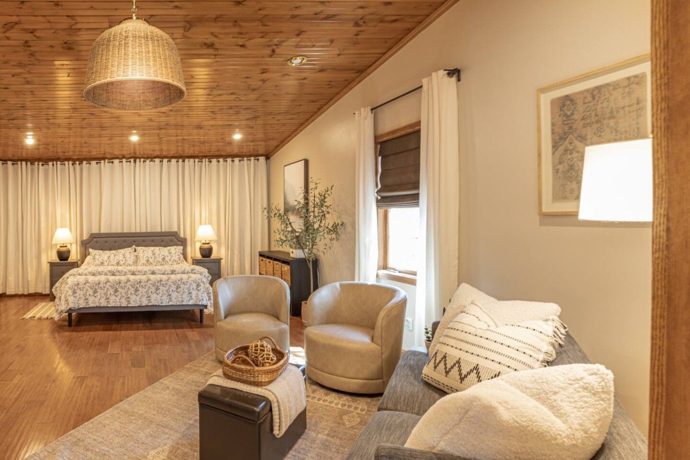 A bedroom with a bed, two armchairs, a sofa, a bedside table, a lamp, a hanging light fixture, and a window with curtains.