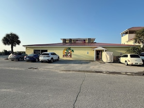 A building with a mural of a turtle, parked cars, and a palm tree. - Fishy Fishy UP - 3BR 1BA duplex home @ Yaupon Oak Island Pier & 801 Event Center (Oak Island)