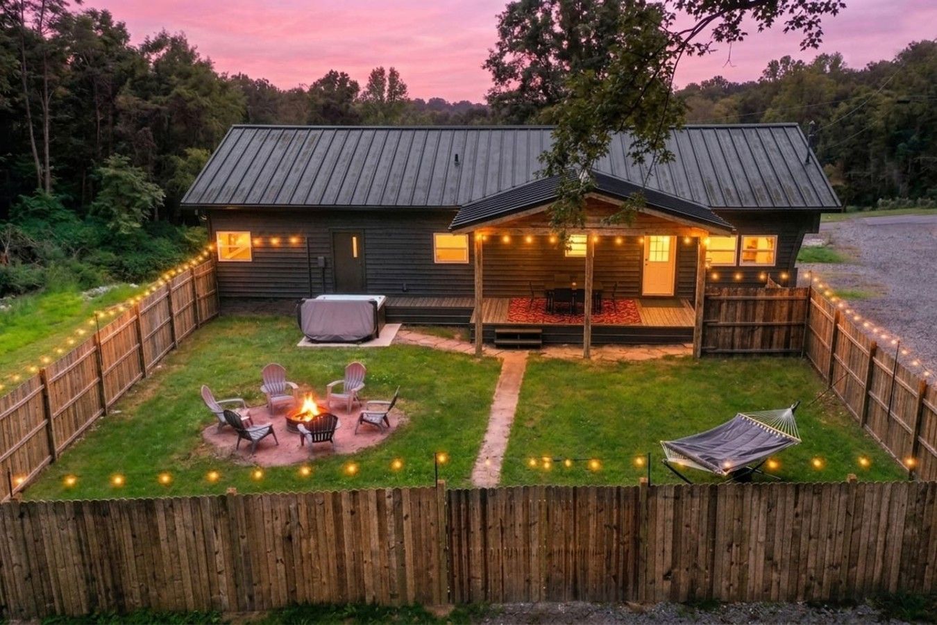 Une cabane en bois avec une cour arrière clôturée, un foyer et des guirlandes lumineuses.