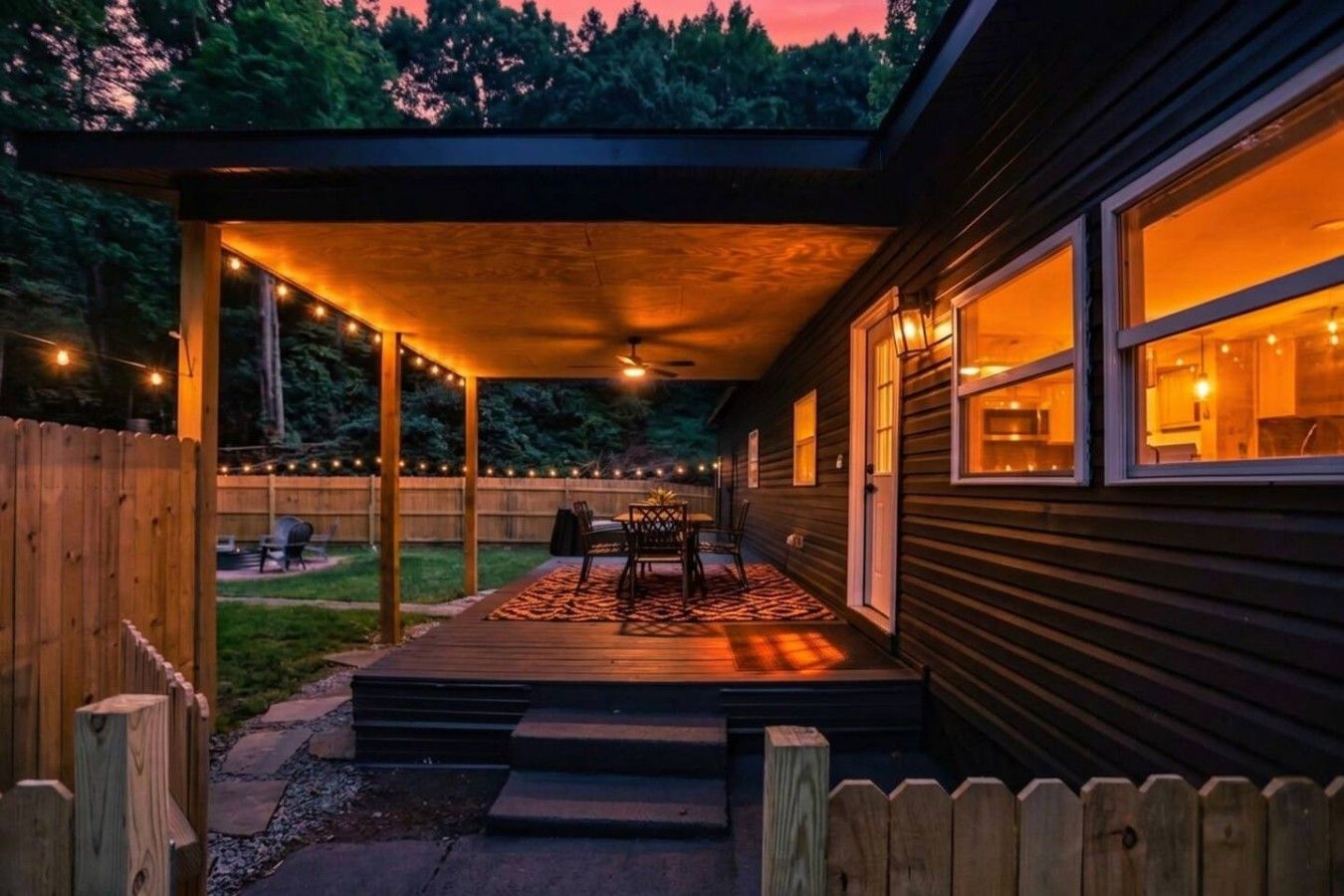 A covered patio area with a table and chairs, a wooden deck, and a view of the backyard.