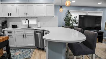 A modern kitchen with white cabinets, a dishwasher, and a dining area with a round table and chairs.