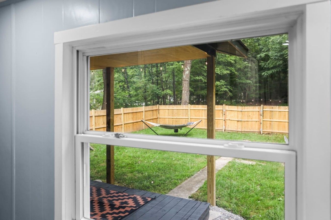 A window with a view of a backyard, including a wooden deck and a hammock.