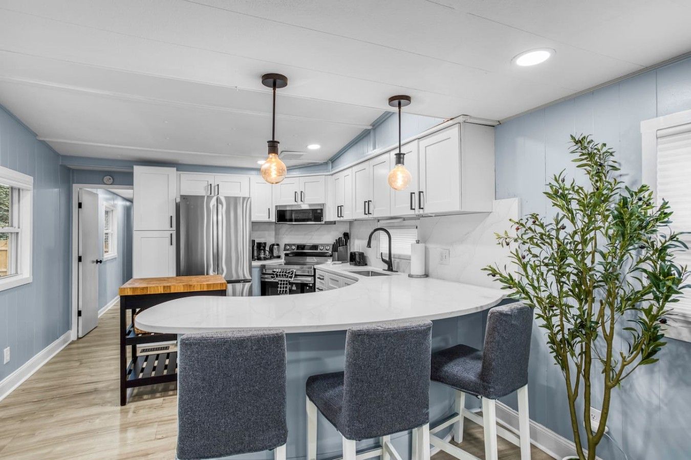 Une cuisine moderne avec des meubles blancs, un îlot central doté de tabourets et un éclairage suspendu.