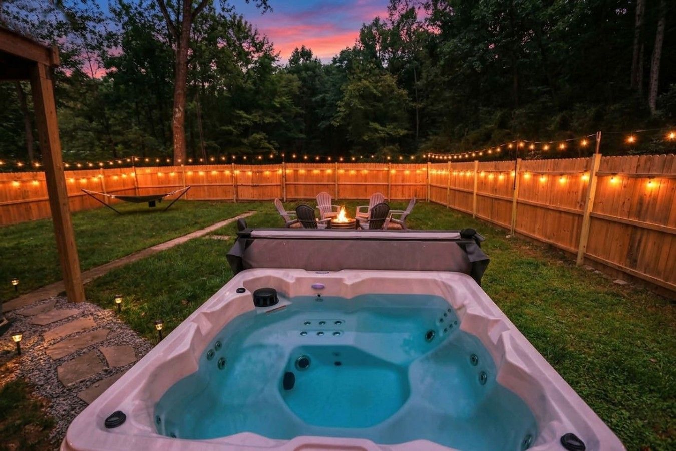 A hot tub in a backyard with a wooden fence and string lights.