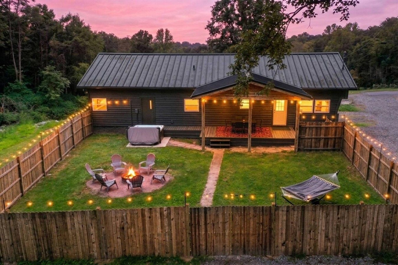 A wooden cabin with a fenced backyard, a fire pit, and string lights.
